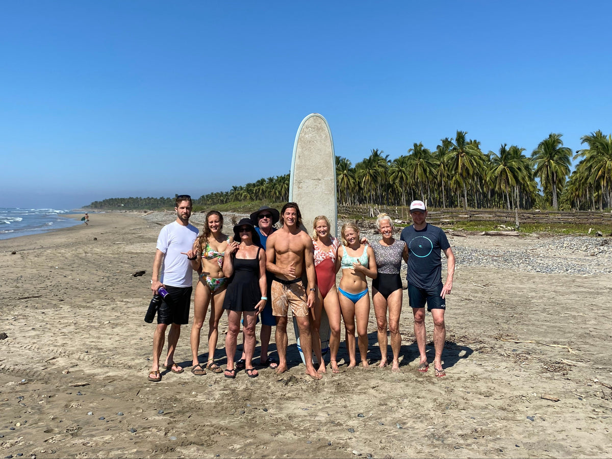 Group of people standing on a beach in troncones, mexico on retreat with a surfboard, palm trees in the background